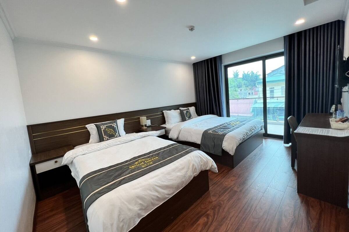 A hotel room with two beds, a desk, and a large window.