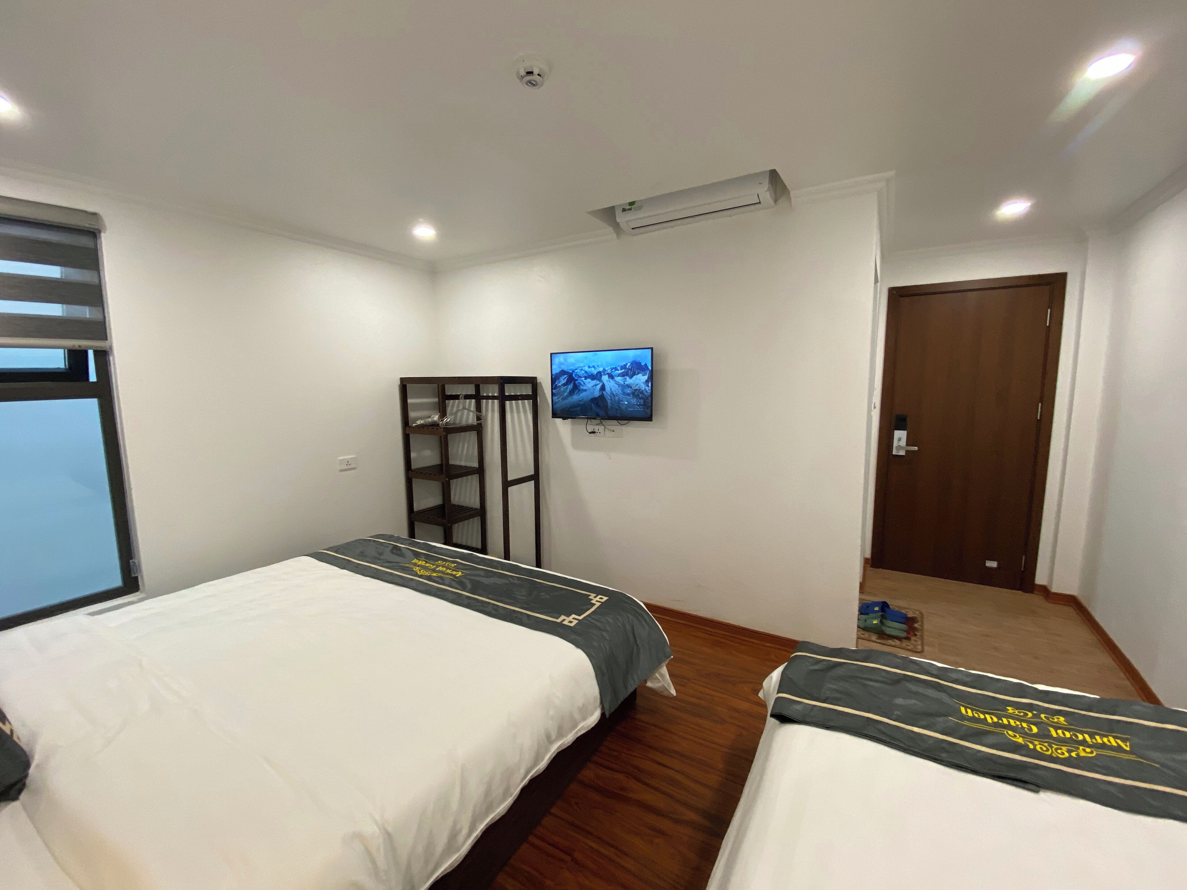 Une chambre d’hôtel avec deux lits, un téléviseur fixé au mur et une armoire en bois.