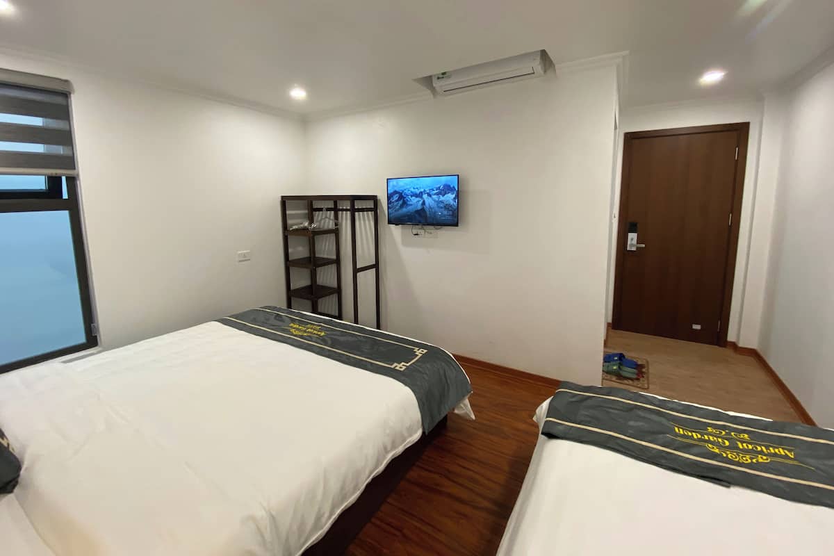 A hotel room with two beds, a TV mounted on the wall, and a wooden wardrobe.