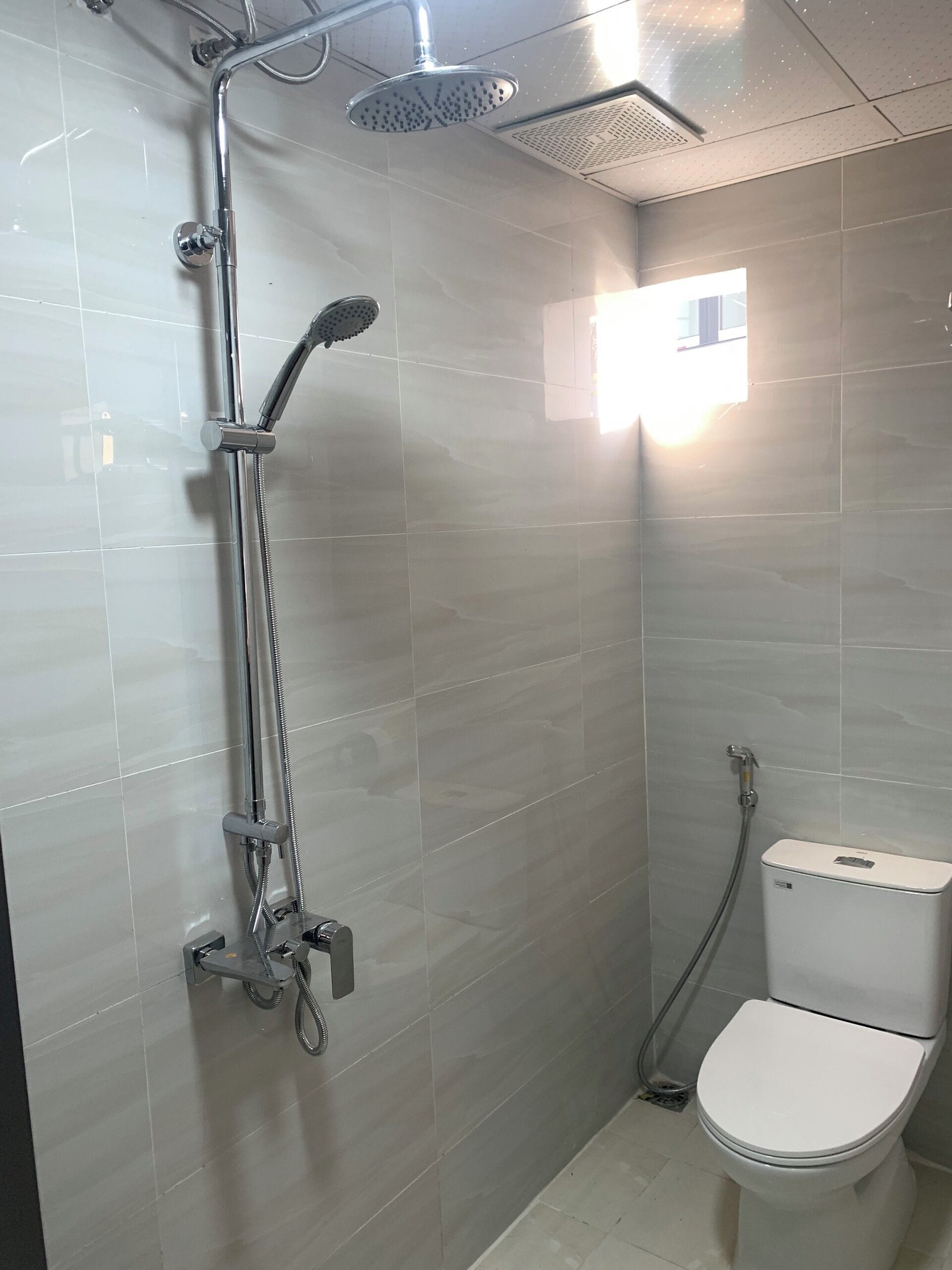 A modern bathroom with a shower, toilet, and a small window providing natural light.