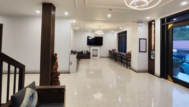 Un vestíbulo de hotel moderno con mostrador de recepción, un televisor montado en la pared, un comedor con sillas y un amplio ventanal con vistas al exterior.