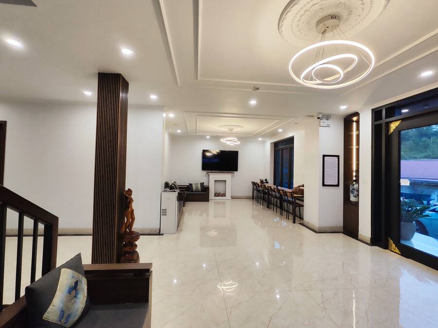 Un vestíbulo de hotel moderno con mostrador de recepción, un televisor montado en la pared, un comedor con sillas y un amplio ventanal con vistas al exterior.