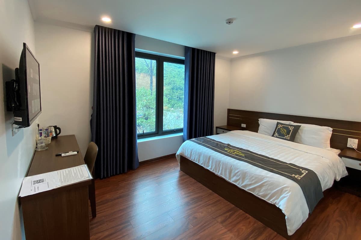 A hotel room with a bed, a desk, a chair, a TV, and a window with curtains.