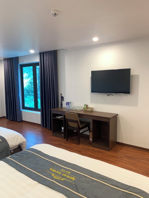 Une chambre d’hôtel avec un lit, un bureau, une chaise, une télévision et une fenêtre avec des rideaux.