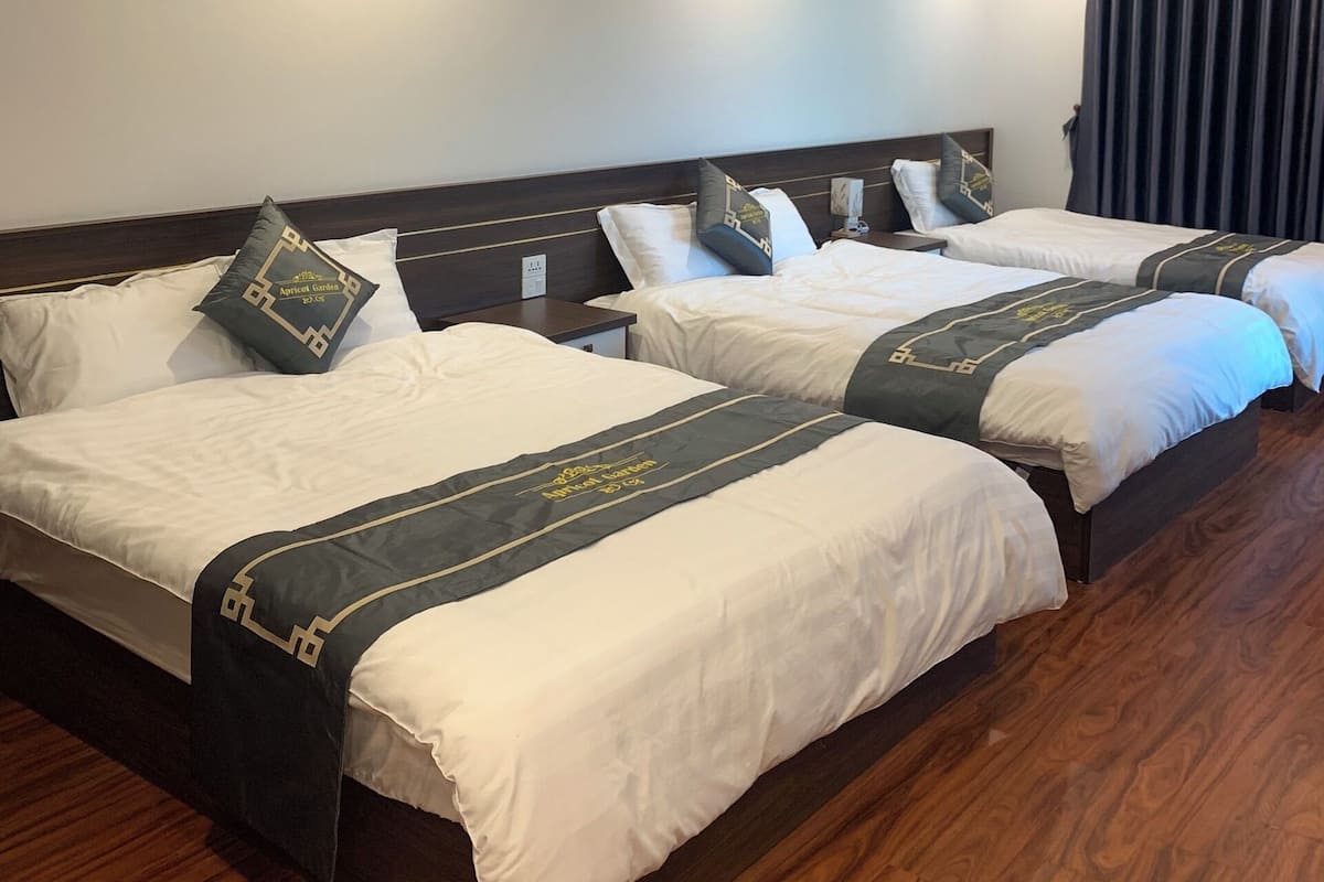 A hotel room with three beds, each with a dark headboard and white bedding.