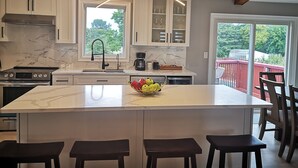 Cozinha moderna com uma ilha grande, armários brancos e vista para um deck vermelho.