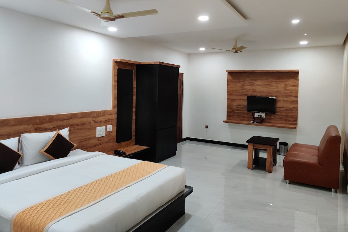 A hotel room with a bed, a TV mounted on the wall, a wardrobe, a desk, and a chair.