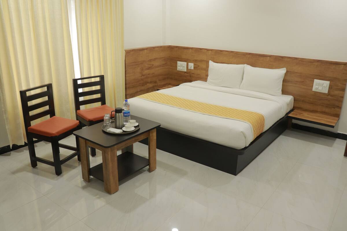 A hotel room with a bed, two chairs, a small table with a water bottle, and a cup.