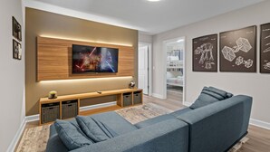 Un salon moderne avec un grand téléviseur à écran plat fixé sur un panneau en bois, un canapé gris et une petite table basse.