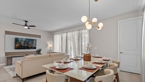 Un espace repas moderne avec une longue table, six chaises et un ventilateur de plafond.