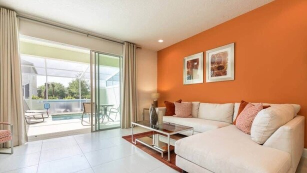 Una sala de estar moderna con un sofá blanco, una mesa de centro de vidrio y vistas a una piscina a través de amplios ventanales correderas.