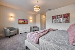 Ein Schlafzimmer mit einem Bett, zwei Stühlen, einer Kommode, einem Gemälde und einer Tür.