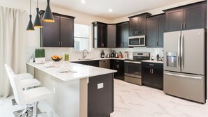 A modern kitchen with dark cabinets, stainless steel appliances, and pendant lighting. - Private Pool, Modern Elegance, Ideal Locale (Davenport)