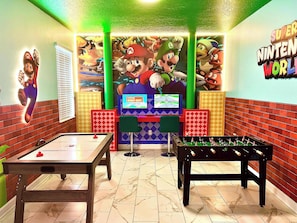 Une salle décorée sur le thème de Mario, avec un baby-foot, une table de billard et un panneau « Nintendo World ».