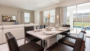 A dining area with a table set for six, a sofa, and a TV on the wall. - Private Pool, Modern Elegance, Ideal Locale (Davenport)