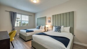Ein Hotelzimmer mit zwei Betten, einem Schreibtisch, einem Stuhl, einem Fenster mit Vorhängen und einer Wandlampe.