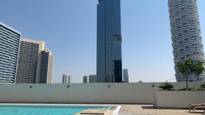 A rooftop pool with a view of a tall skyscraper and a cylindrical building. - NEW Direct Golf View Sport City 2BD (Dubai)