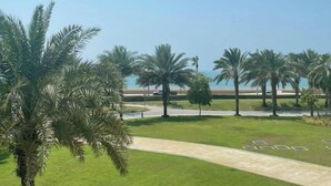 A landscaped area with palm trees, a paved walkway, and a view of the sea. - NEW Direct Golf View Sport City 2BD (Dubai)
