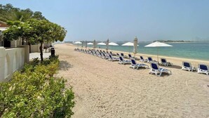 A beach with rows of sun loungers and umbrellas, a clear sky, and a calm sea. - NEW Direct Golf View Sport City 2BD (Dubai)