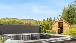 Un jacuzzi con terraza de madera, rodeado de vegetación y una estructura de madera al fondo.