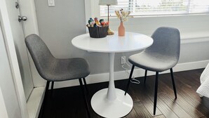 A small room with two grey chairs, a white table, and a lamp. There is a window with blinds, and a door is visible on the left. - Jennifers House (Vancouver)