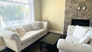 A living room with a beige sofa, a patterned throw pillow, a dark coffee table, and a stone fireplace. - Jennifers House (Vancouver)