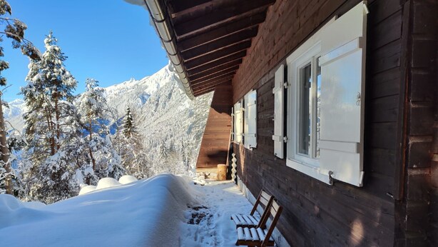 A wooden cabin with a snow-covered porch, a bench, and a mountain backdrop. - Lieblingsplatz by Interhome (Flirsch)