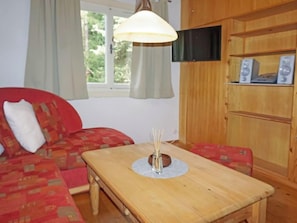 A cozy living room with a wooden table, a red sofa, and a television mounted on the wall.