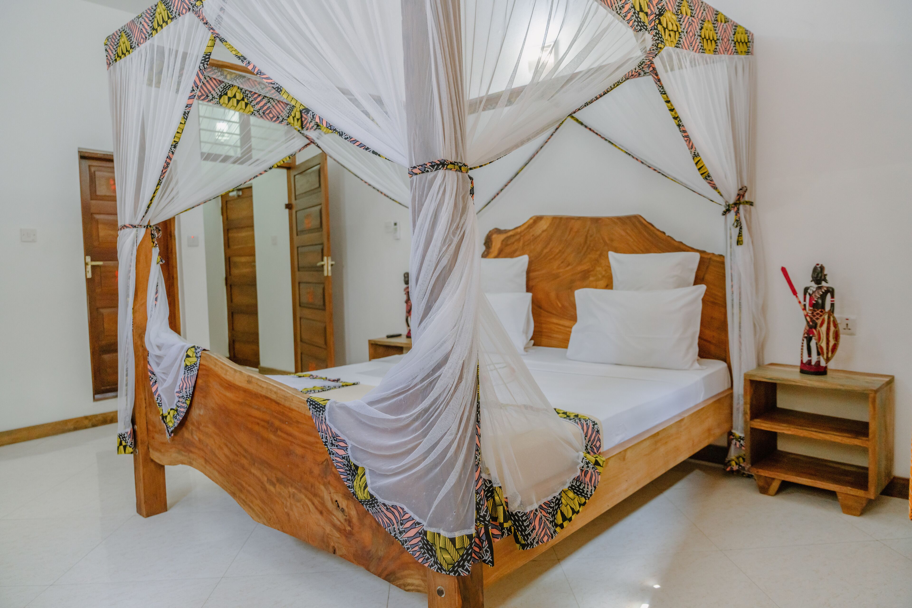 A wooden bed with a canopy, white bedding, and a nightstand with a decorative item.