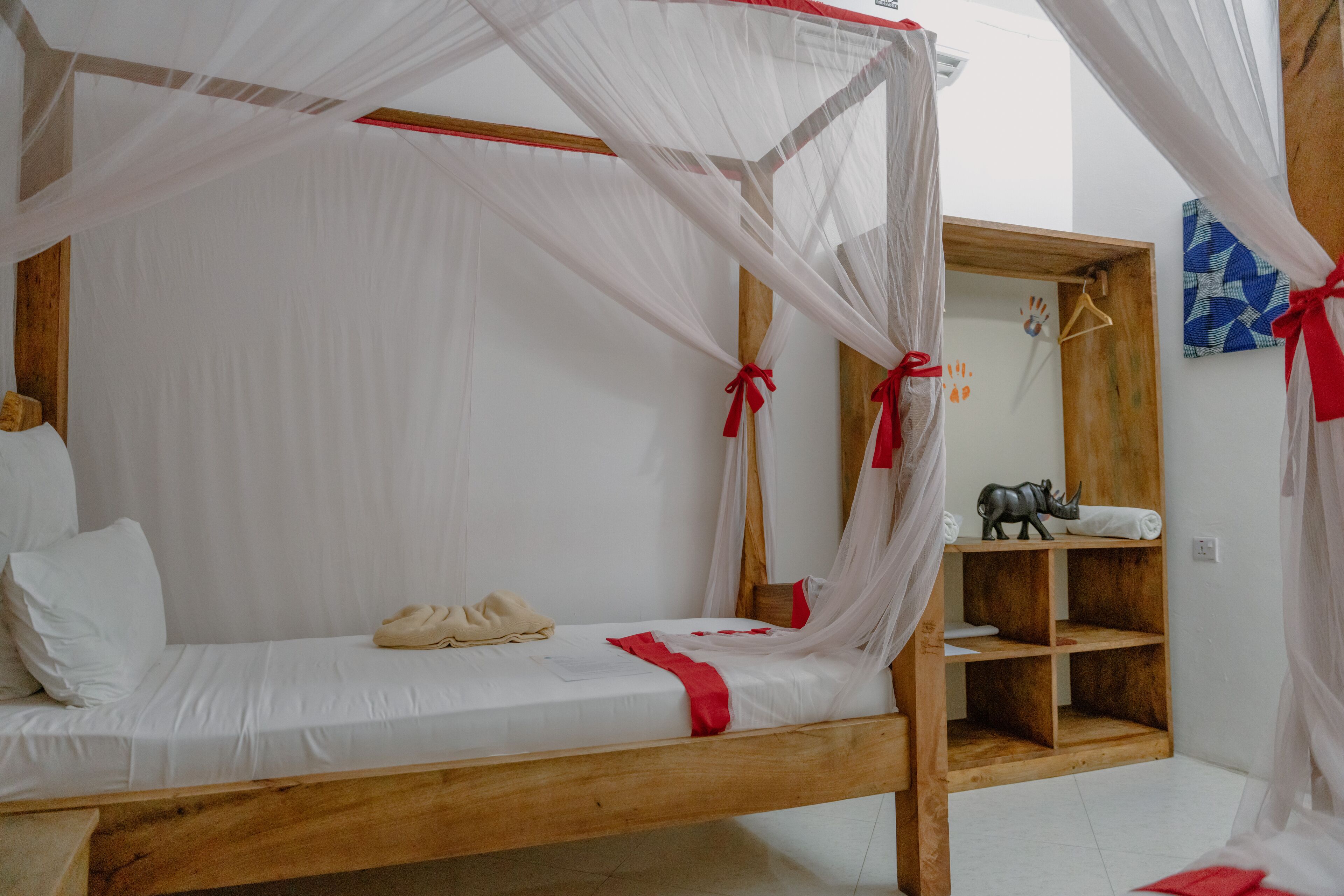 A single bed with a wooden frame, white bedding, and a canopy with red ties.