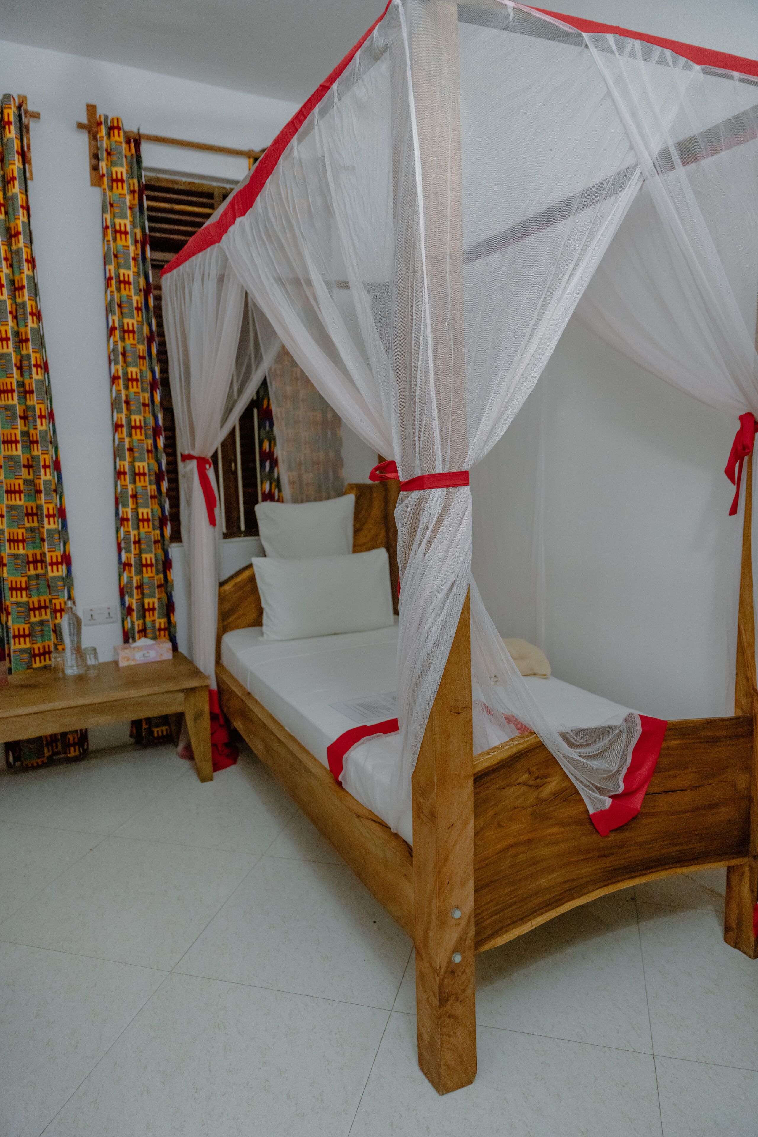 A wooden bed with a canopy, white bedding, and red accents.