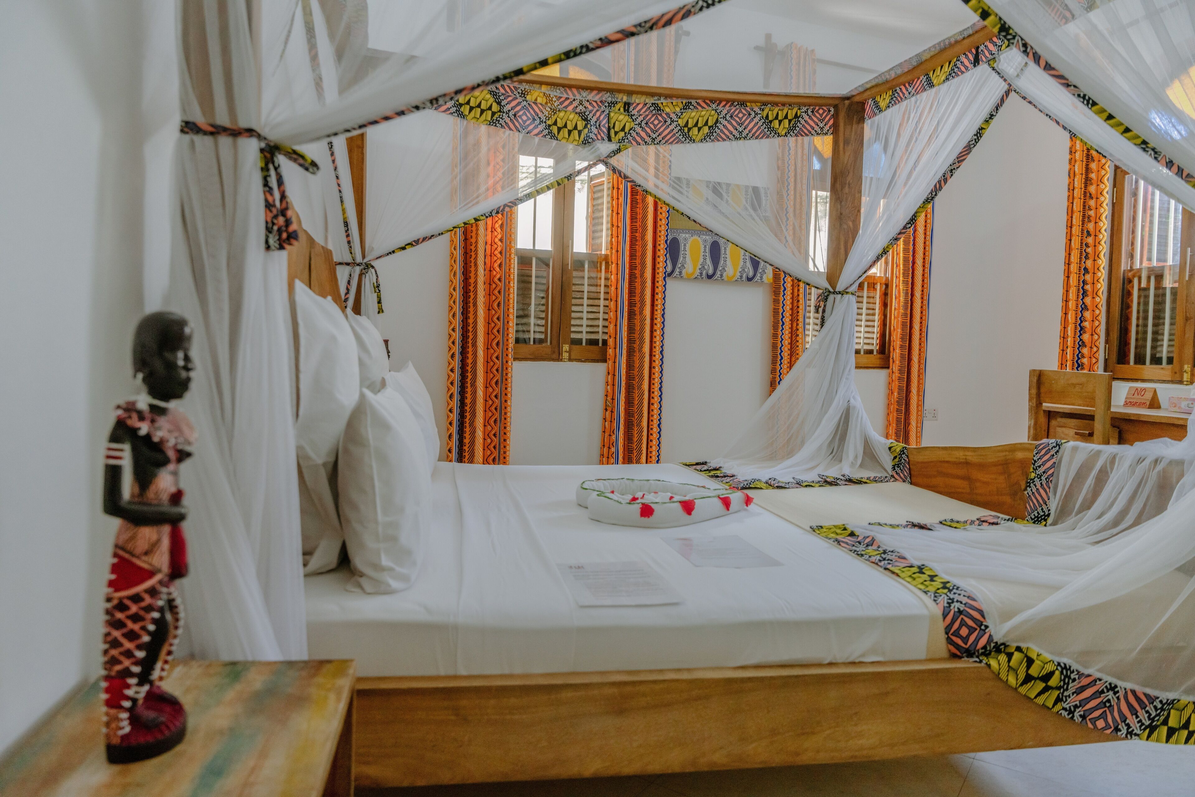 A room with a bed covered in white sheets, a wooden headboard, and a canopy with colorful patterns.