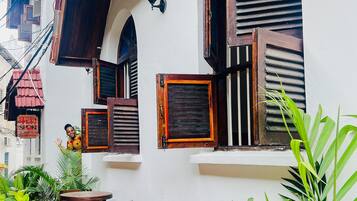 Un bâtiment traditionnel avec des volets en bois, un balcon agrémenté de meubles en bois et une végétation luxuriante.