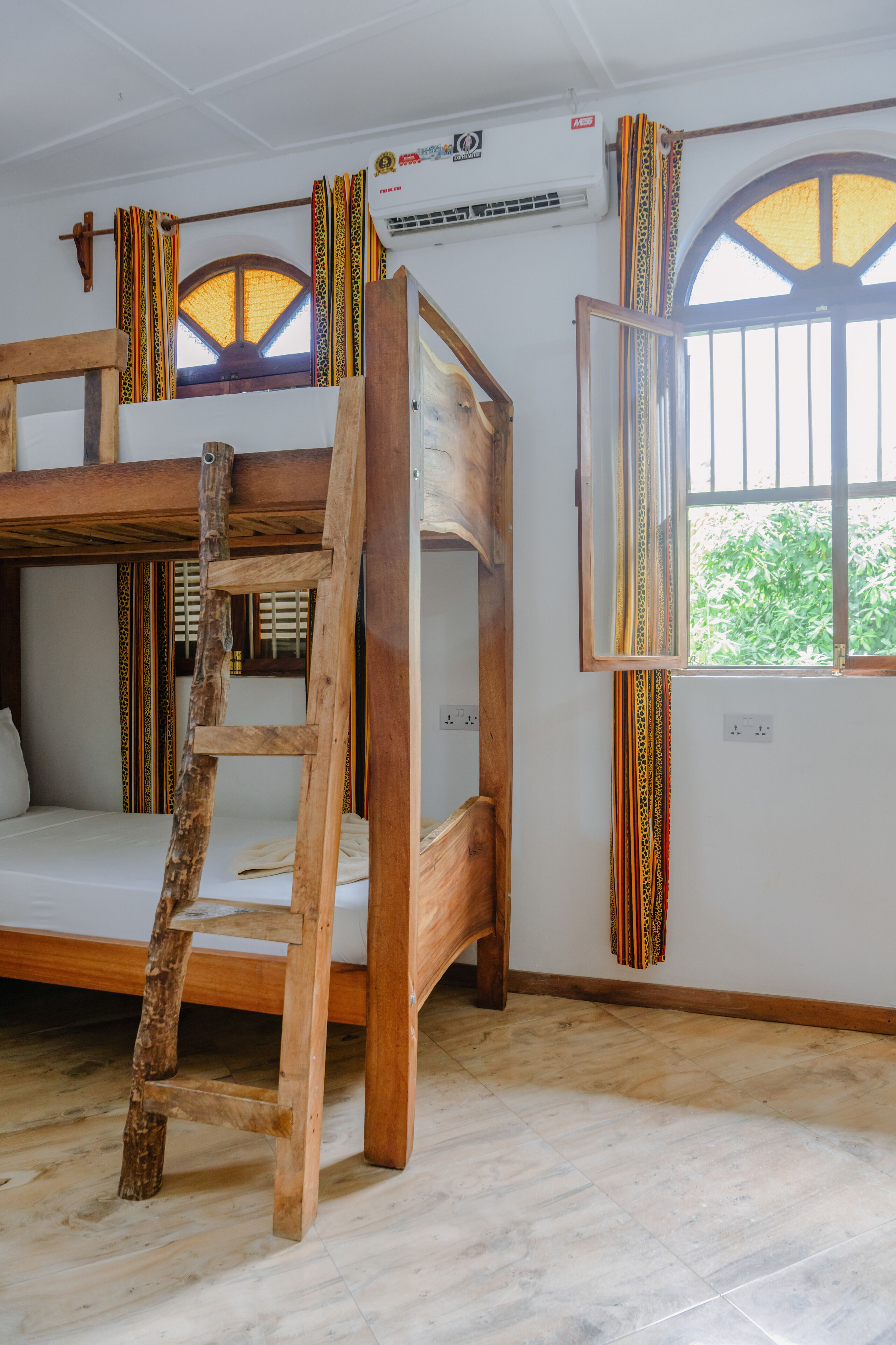 A room with a bunk bed, a wooden ladder, a window with curtains, and an air conditioning unit.
