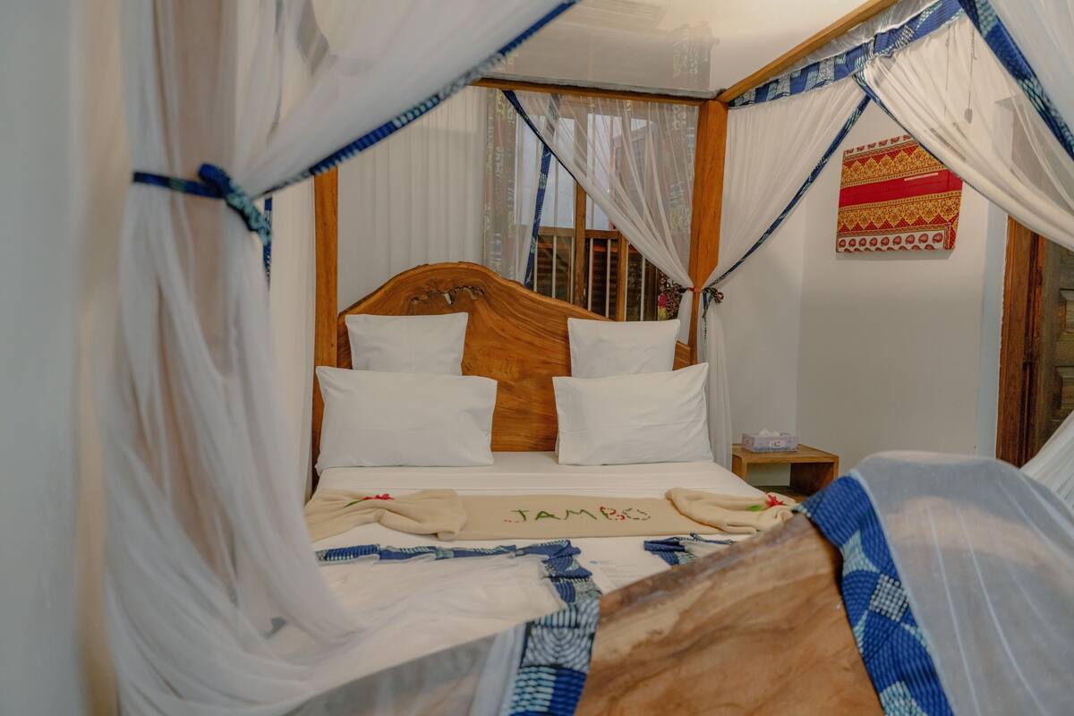 Un lit à baldaquin, une tête de lit en bois et une table de chevet avec une lampe.