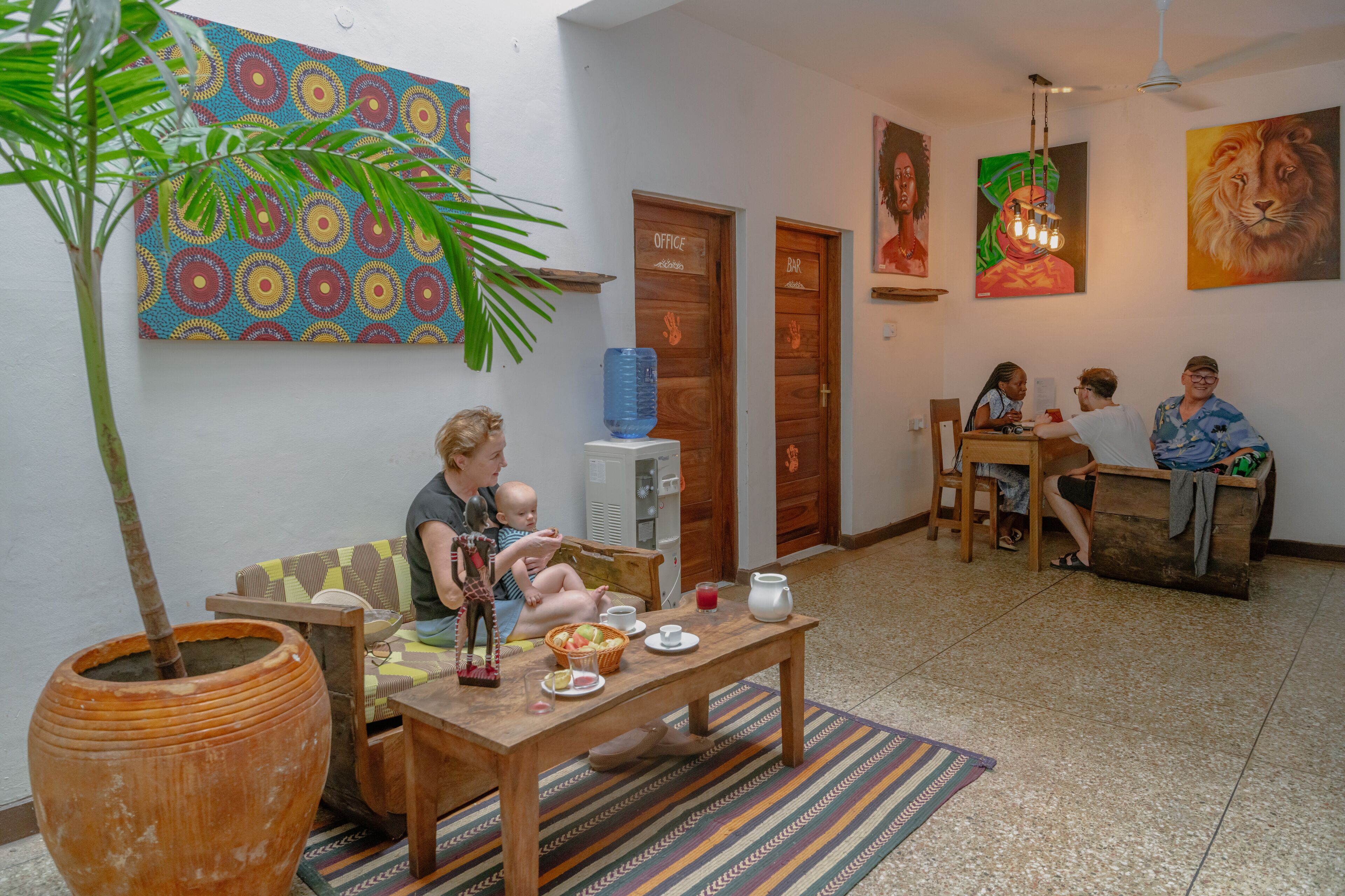 A living room with a sofa, a coffee table, and a potted plant. There are two doors labeled "Office" and "Bar".
