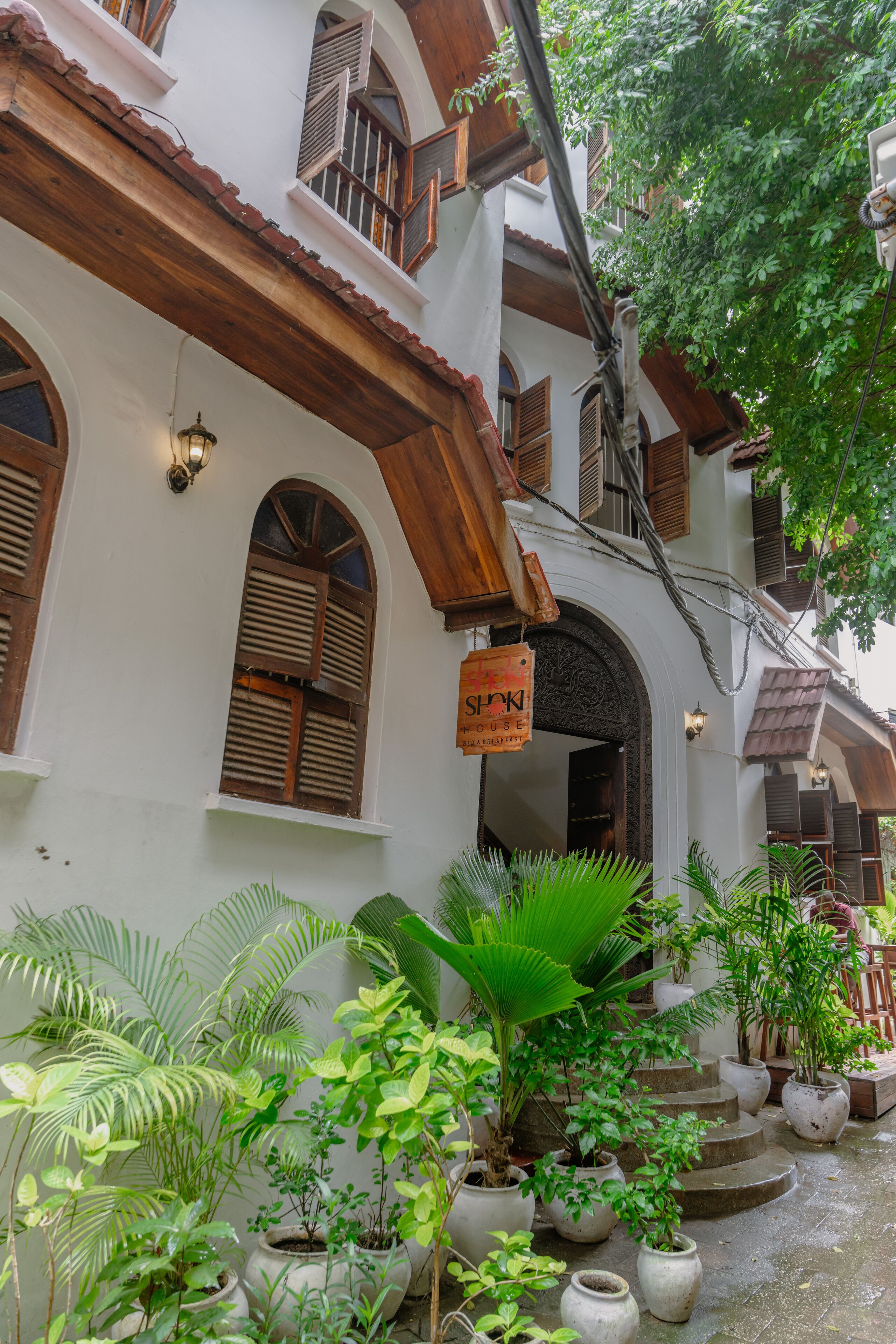 Un edificio tradicional con fachada blanca, balcones de madera y un letrero colgado en la entrada.