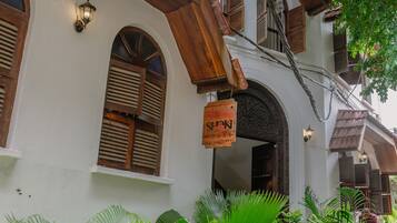 Un edificio tradicional con fachada blanca, balcones de madera y un letrero colgado en la entrada.