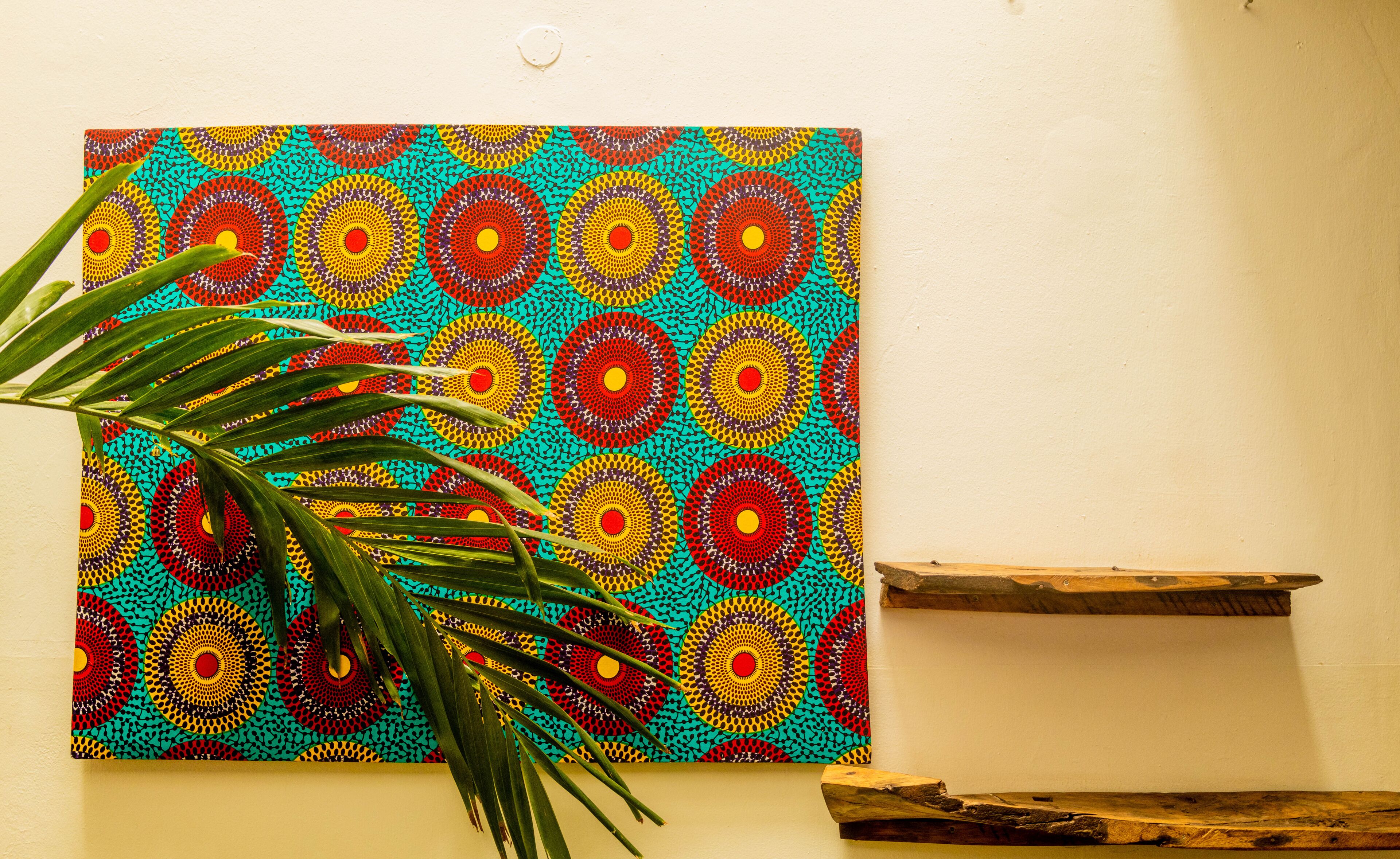 A vibrant artwork with a circular pattern on a wall, a wooden shelf, and a potted plant.