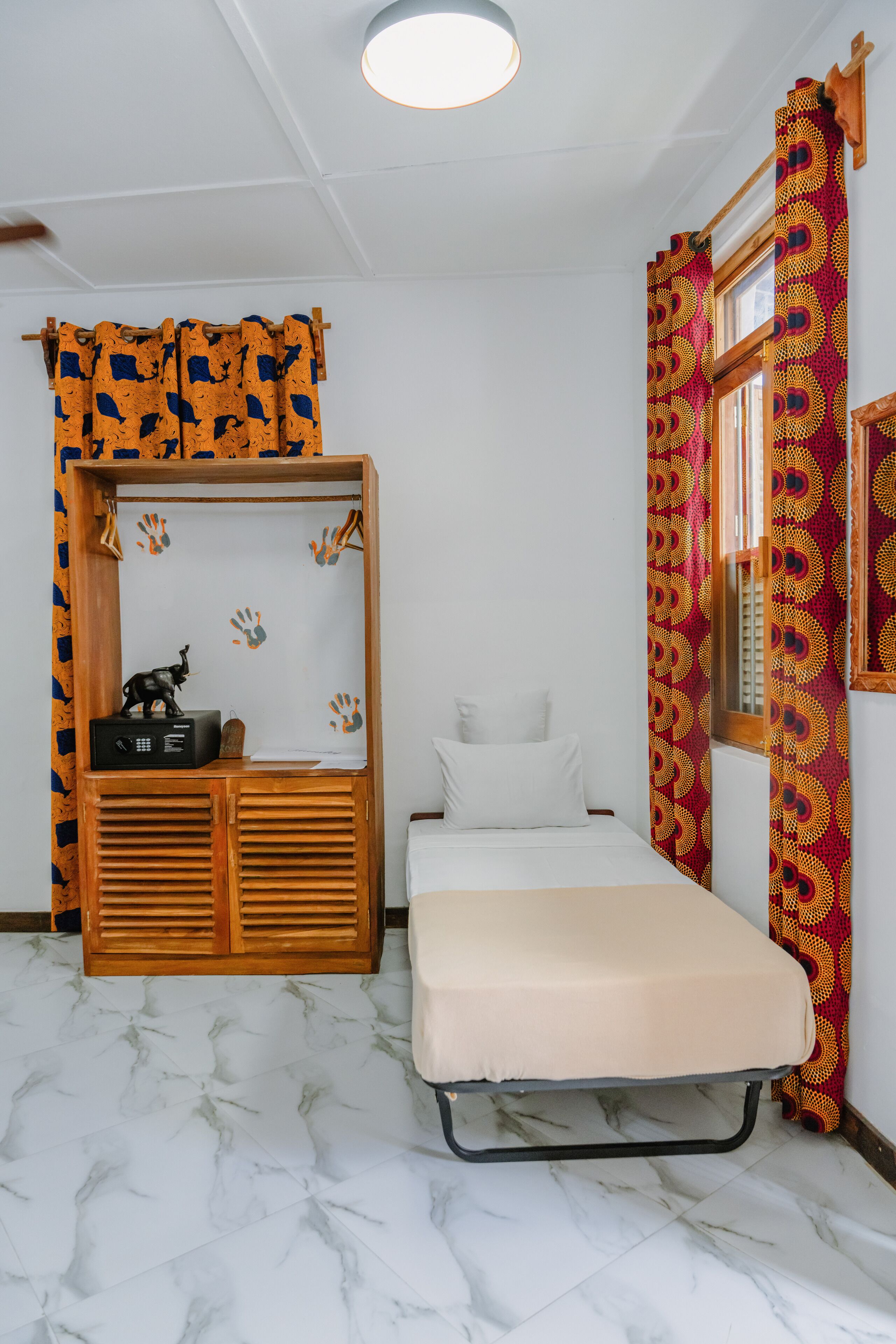 A bedroom with a bed, a wooden wardrobe, and a window with patterned curtains.