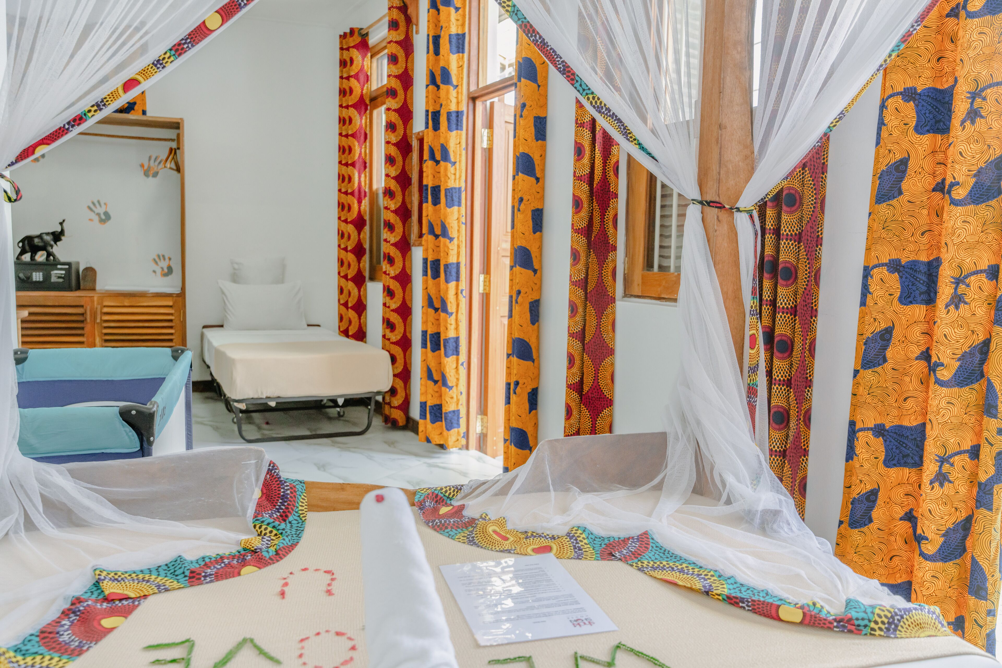 Ein Zimmer mit einem Bett, einem Sessel, einem Schreibtisch und Vorhängen mit bunten Mustern.