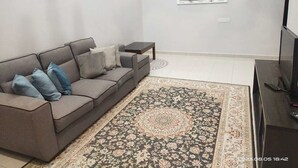 Una sala moderna con un sofá gris, un tapete estampado, una mesita auxiliar, un televisor y un espejo fijado a la pared.