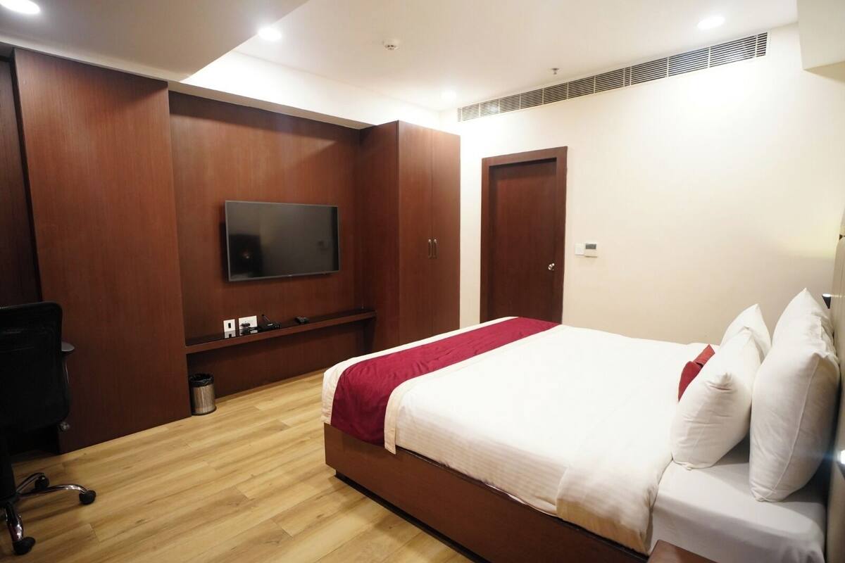 Une chambre d’hôtel avec un lit, un téléviseur fixé au mur, des armoires en bois et un bureau avec une chaise.