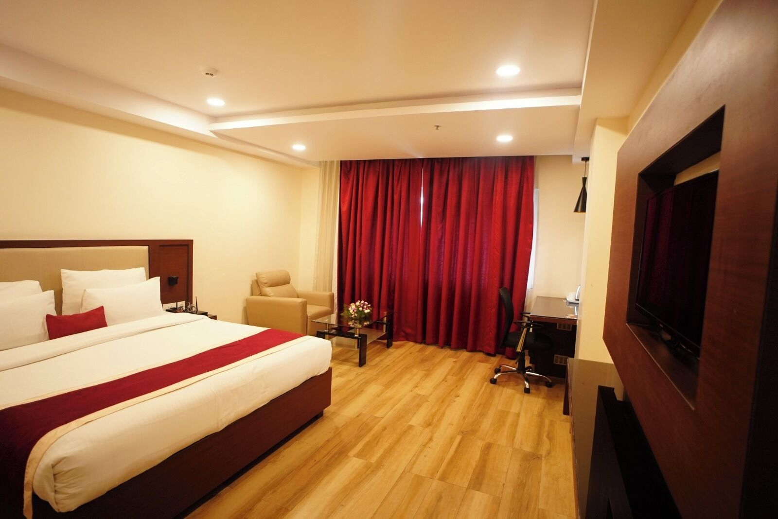 A hotel room with a large bed, a desk, a chair, a TV, and red curtains.