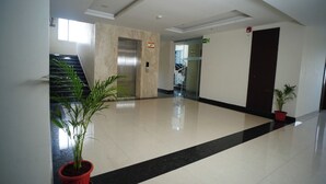 A clean, modern lobby with a polished floor, a staircase, an elevator, and potted plants.