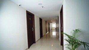 A long, narrow hallway with doors on both sides, a tiled floor, and a potted plant on the right.