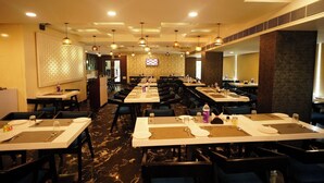 A hotel dining area with multiple tables and chairs, ceiling lights, and a patterned wall.