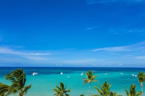 Une plage tropicale aux eaux turquoise et limpides, bordée de palmiers et parsemée de bateaux.