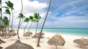Una spiaggia con palme e ombrelloni di paglia.
