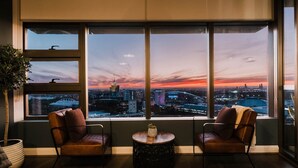 Una habitación con dos sillones de cuero frente a un amplio ventanal con vistas a la ciudad al atardecer.